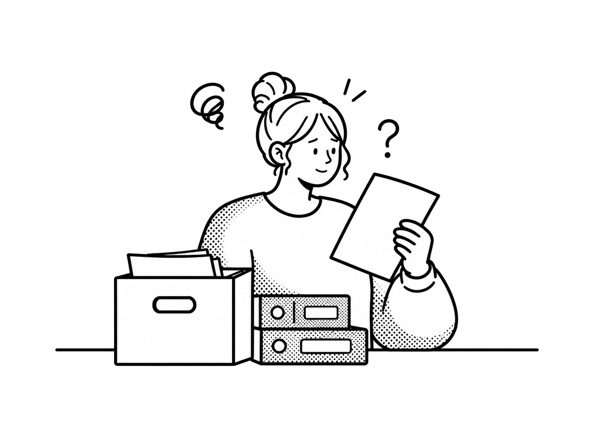 段ボール箱とファイルを前に、書類を見て首をかしげている担当者